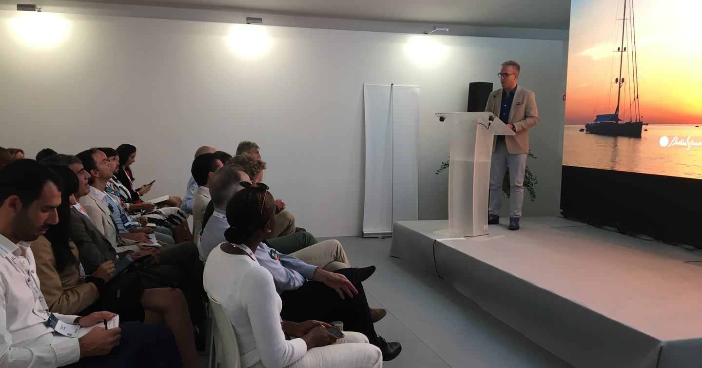 Side view of the Sustainability Conference at the Monaco Yacht Show. Speaker at podium talking to small seated audience.