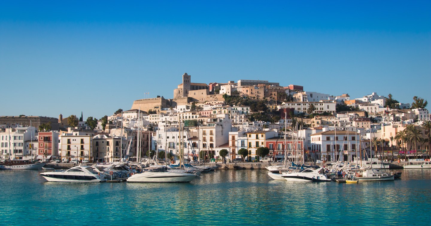 Overview of a marina in Ibiza. Multiple sailing boats and motor yachts moored.