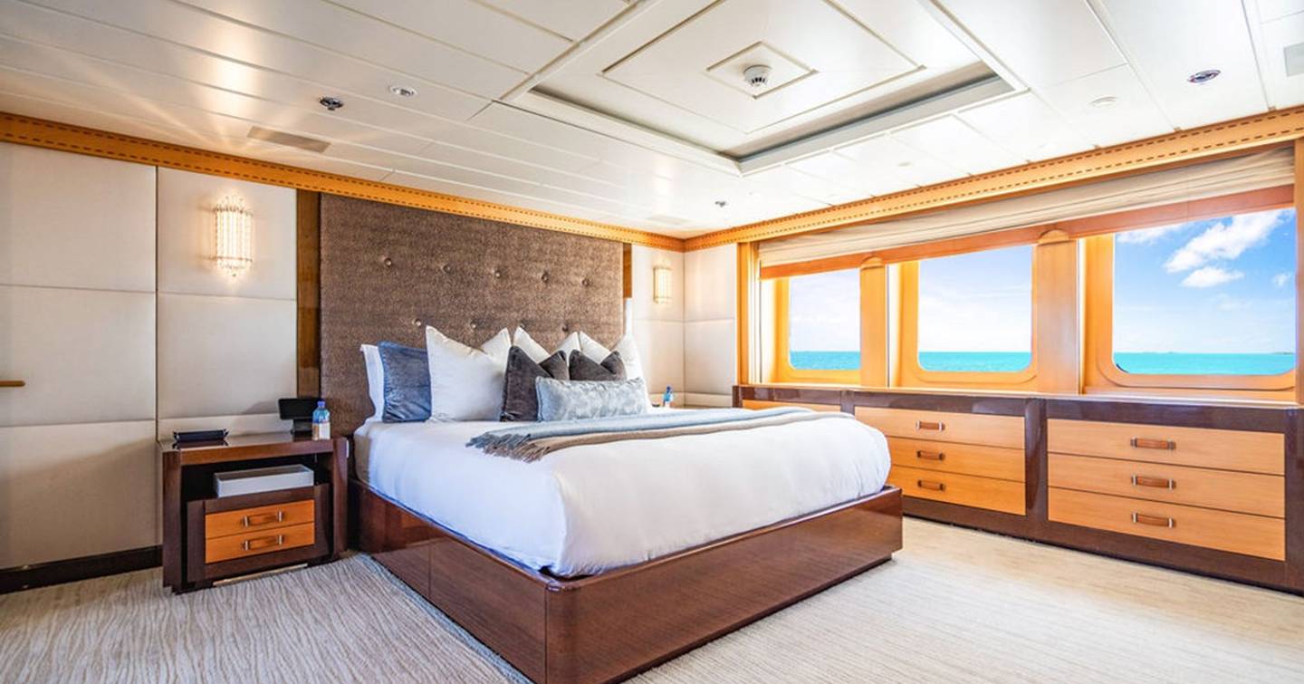 Motor yacht Nita K's bright stateroom with large windows, double bed, wooden cabinetry, and ocean views under a blue sky with clouds