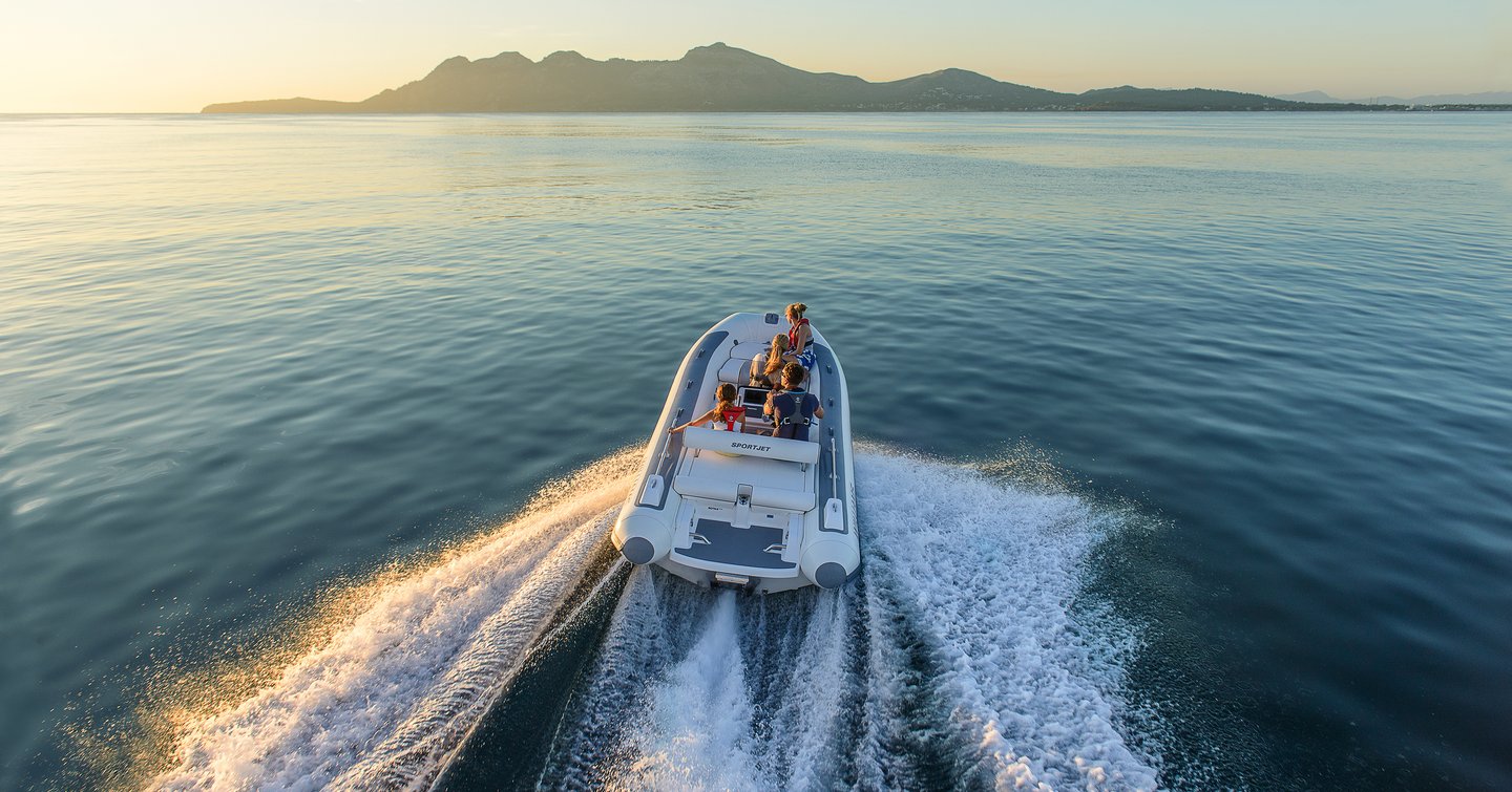 View from behind of a jet tender at sunset heading towards hilly coastline in distance