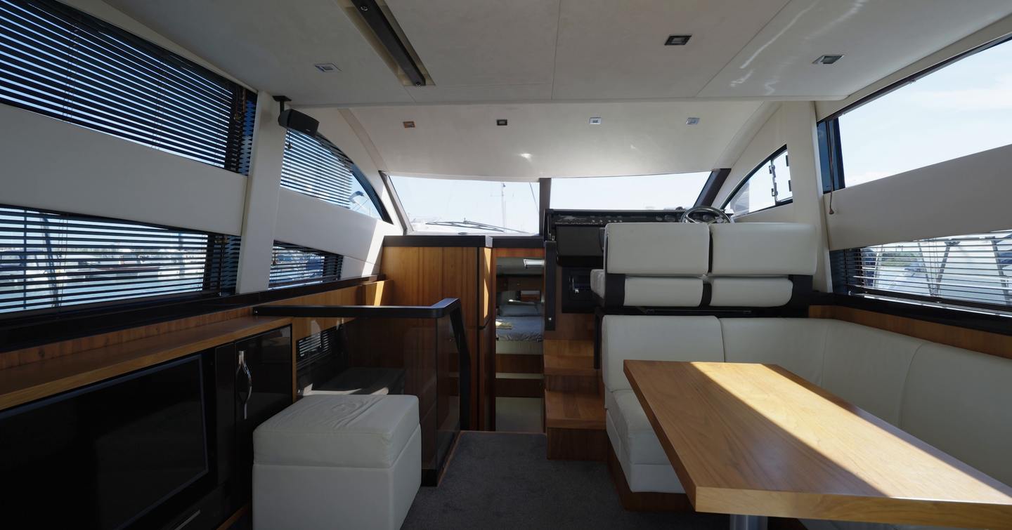 Fairline Squadron 42 saloon with cream leather seating, dining table, timber cabinetry, television and steps leading towards the raised helm during YachtBuyer's £300,000 used boat challenge.
