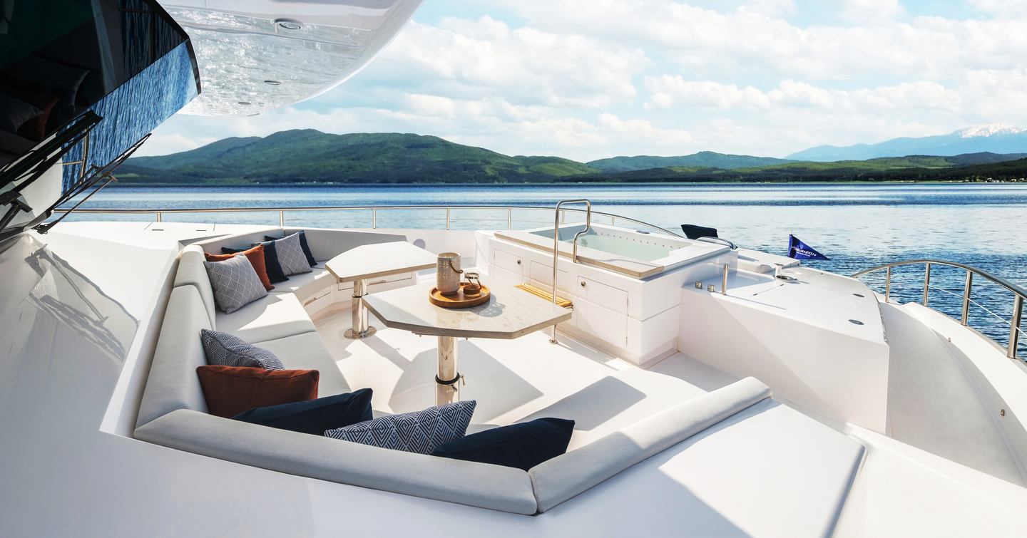 Exterior living area onboard Horizon FD110 Tri-deck. Angular seating surrounds a table overlooking a Jacuzzi.