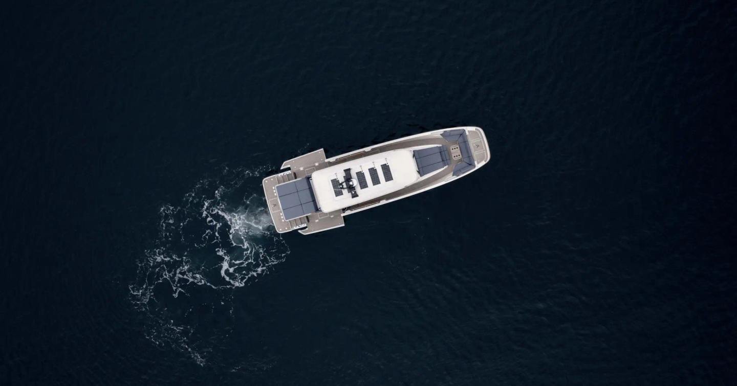 Overhead drone view of the AIATA Sunfinder 50 underway with fold-down side balconies deployed, revealing the wide cockpit terrace and open aft deck layout.