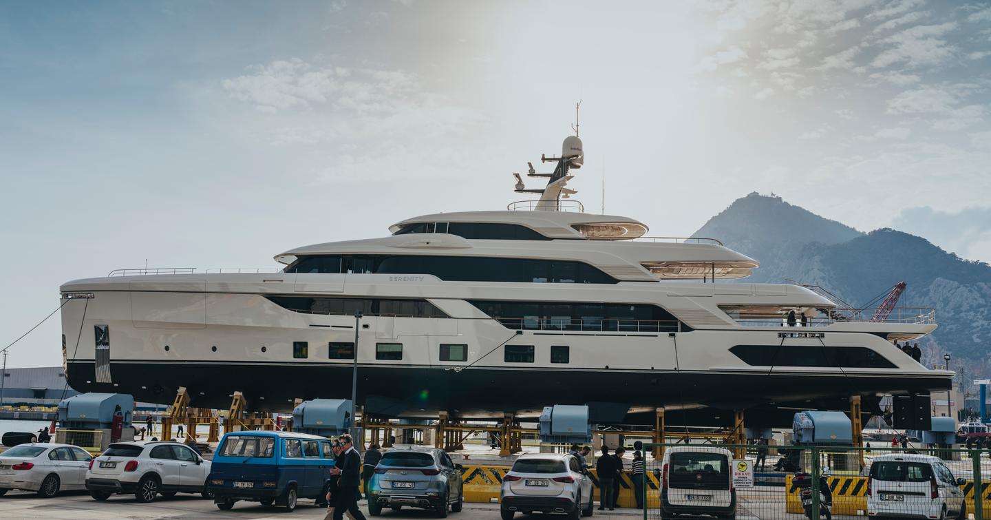 Superyacht Serenity II about to launch with workers and cars with mountains in the background