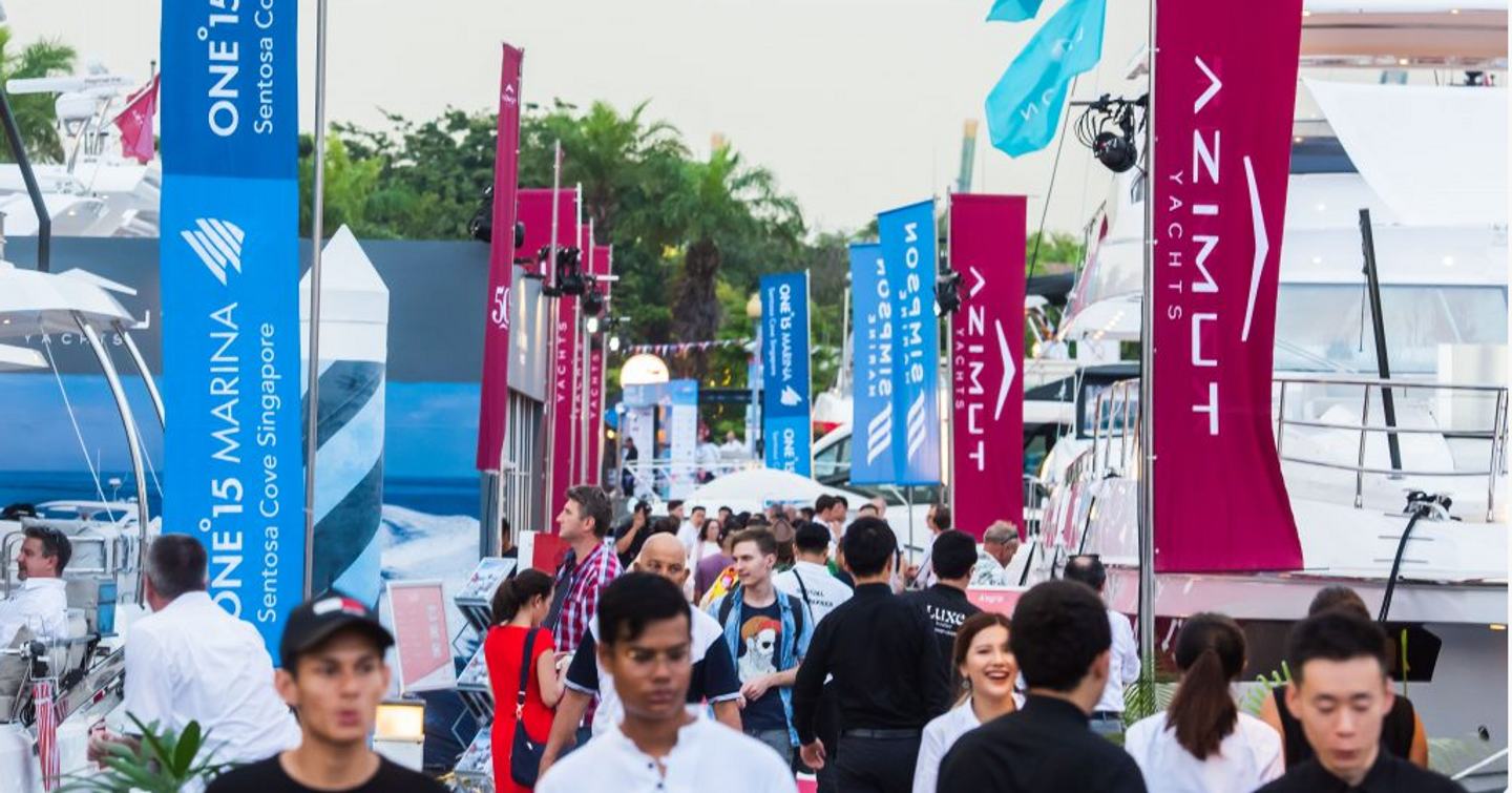 Flags and exhibitors at Singapore Yacht Show, visitors walking along pontoon in between yachts on both sides.