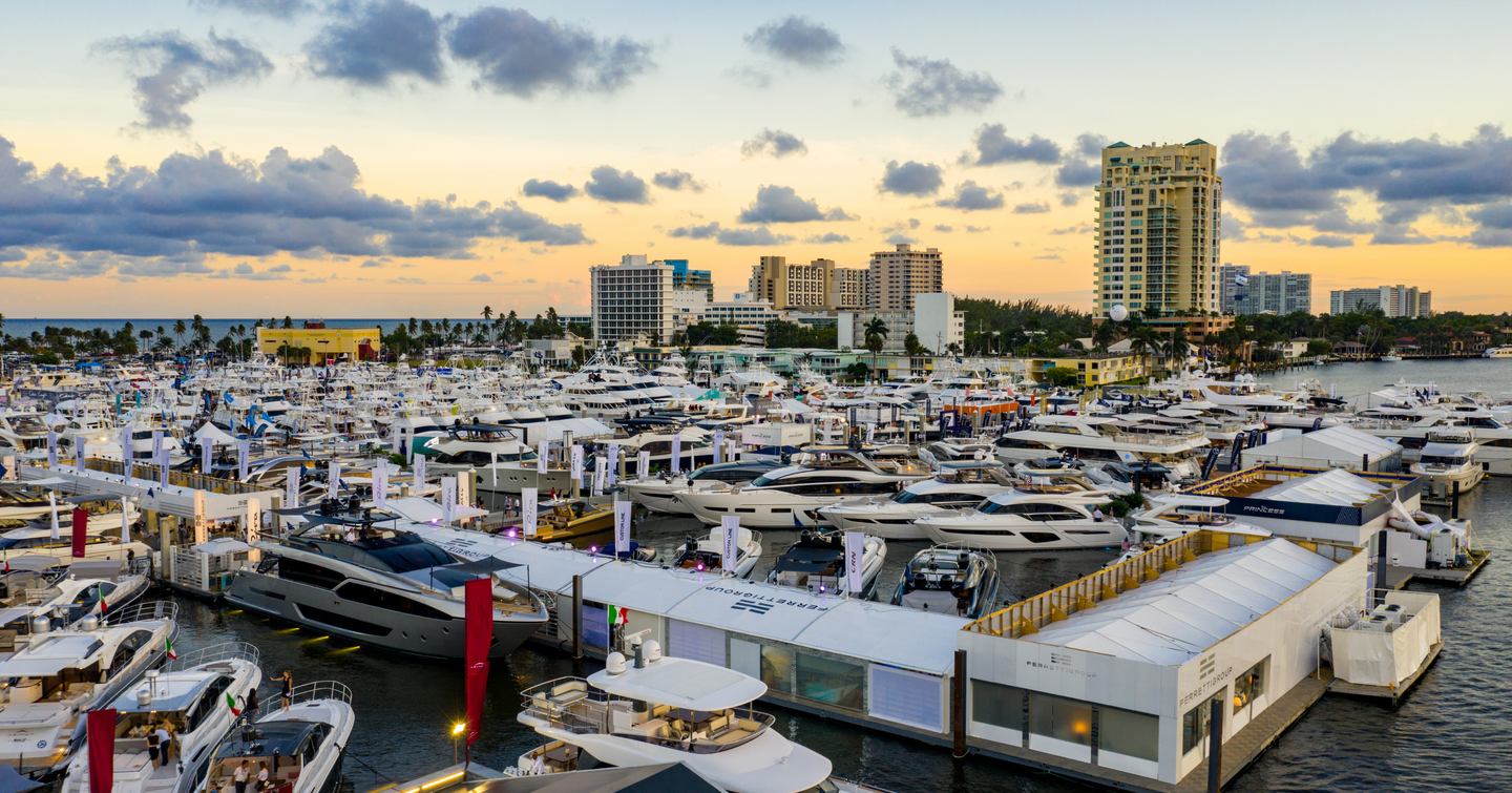 Overview image of FLIBS at dusk, hundreds of yachts moored, surrounded by white gazebos and towering infrastructure in background