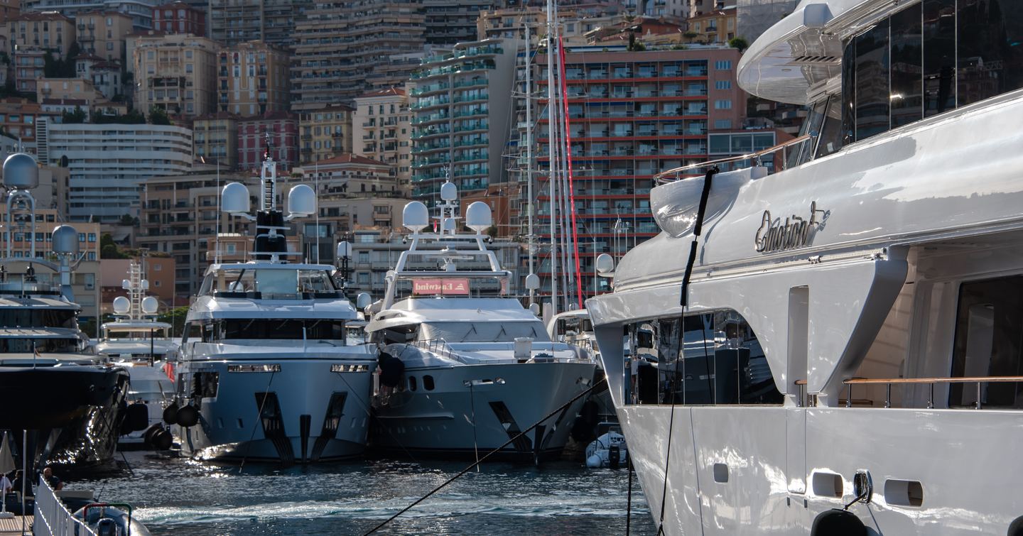 Superyachts moored at Port Hercule during Monaco Yacht Show, with Monte Carlo visible in background.