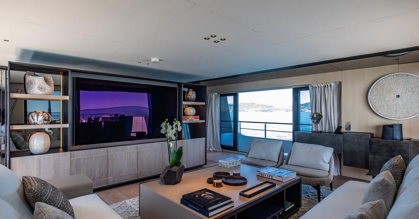 Superyacht Andala upper deck salon with L-shaped grey sofa and mounted TV