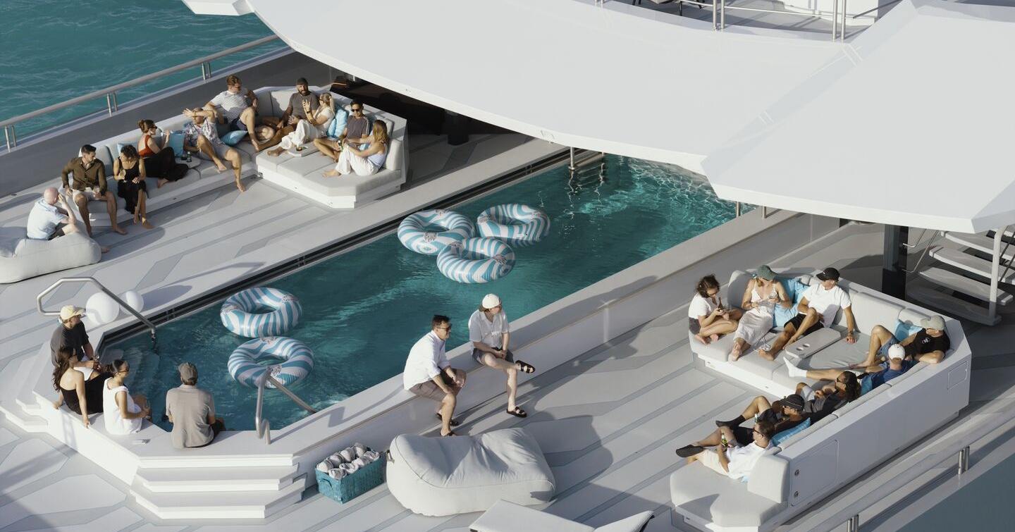 Crew relaxing on Oceanco superyacht Leviathan aft with grey sofas and large swimming pool