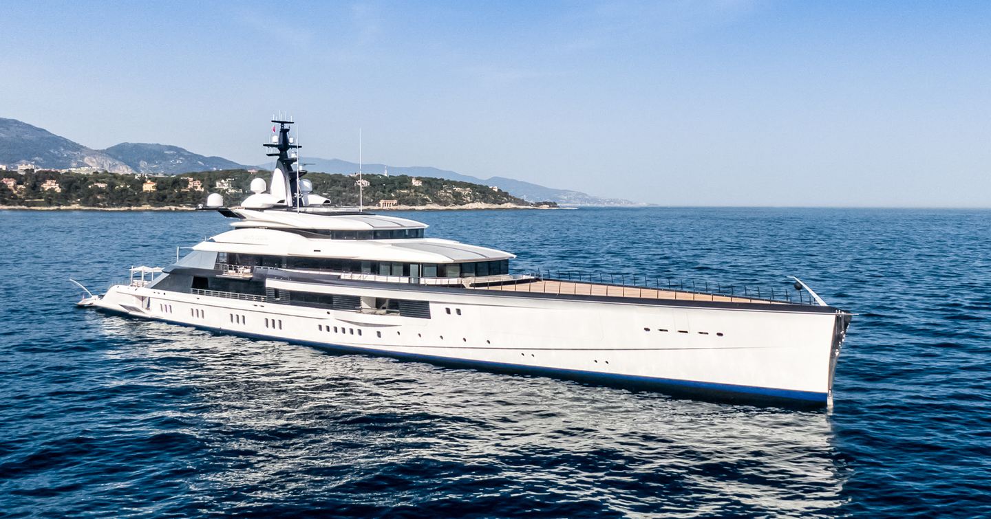 Oceanco Yacht BRAVO EUGENIA shown mid aerial towards starboard bow and along side profile; yacht is stationary in calm waters on bright day, land in background