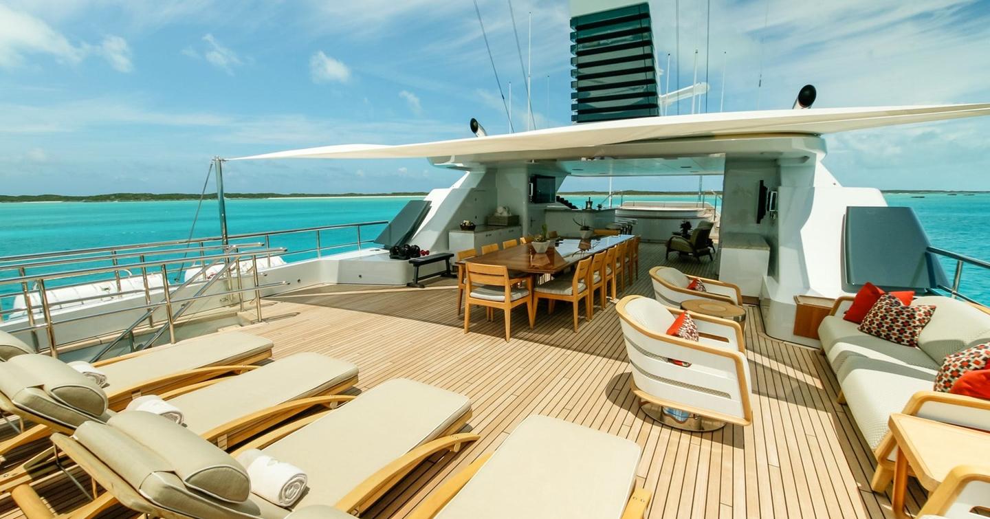 Motor yacht W's sundeck with lounge chairs, dining table and  ocean views under a partly shaded canopy