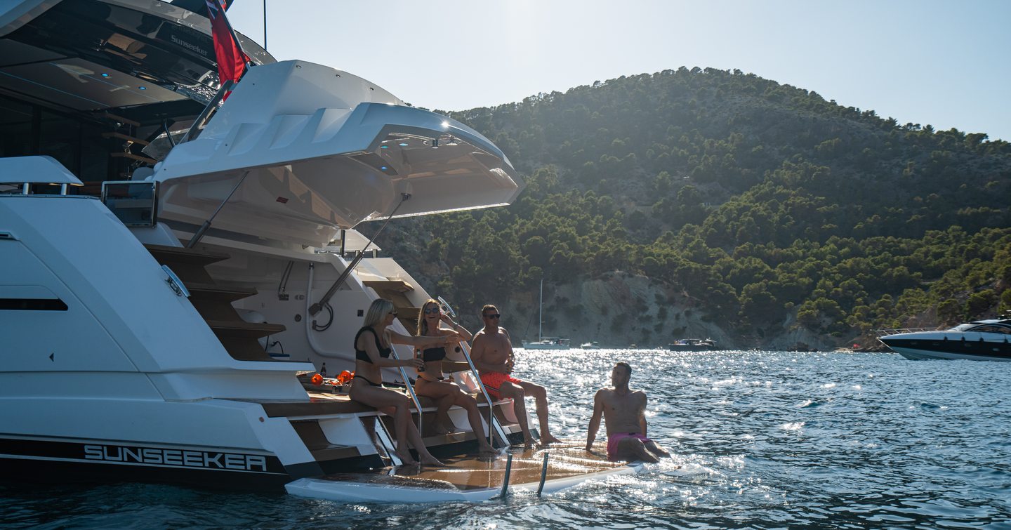  Group of four sat on edge of 65 Sport Yacht with clear water nearby and coast in background