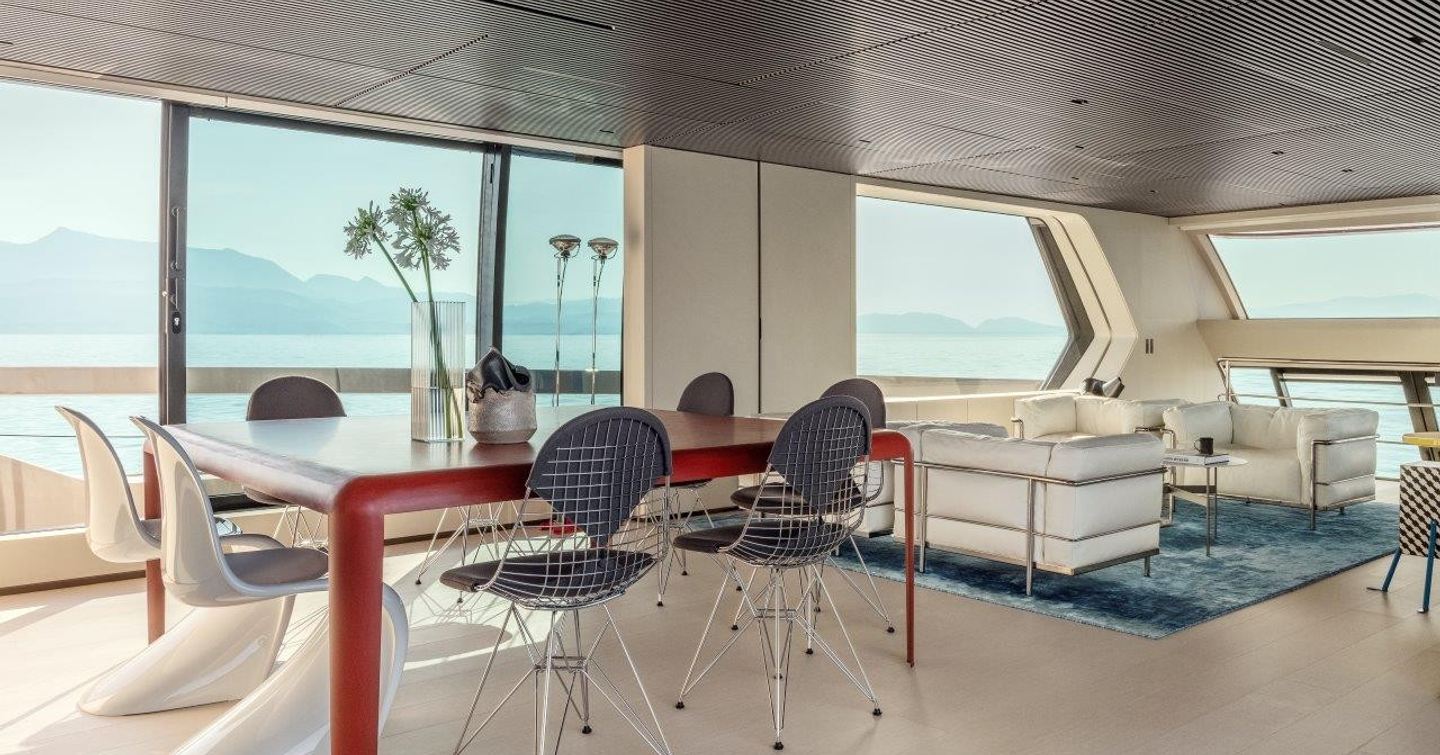 Overview of the main salon onboard the Sanlorenzo SP110. Relaxed dining area in foreground with lounge and white seating behind. Surrounded by large windows.