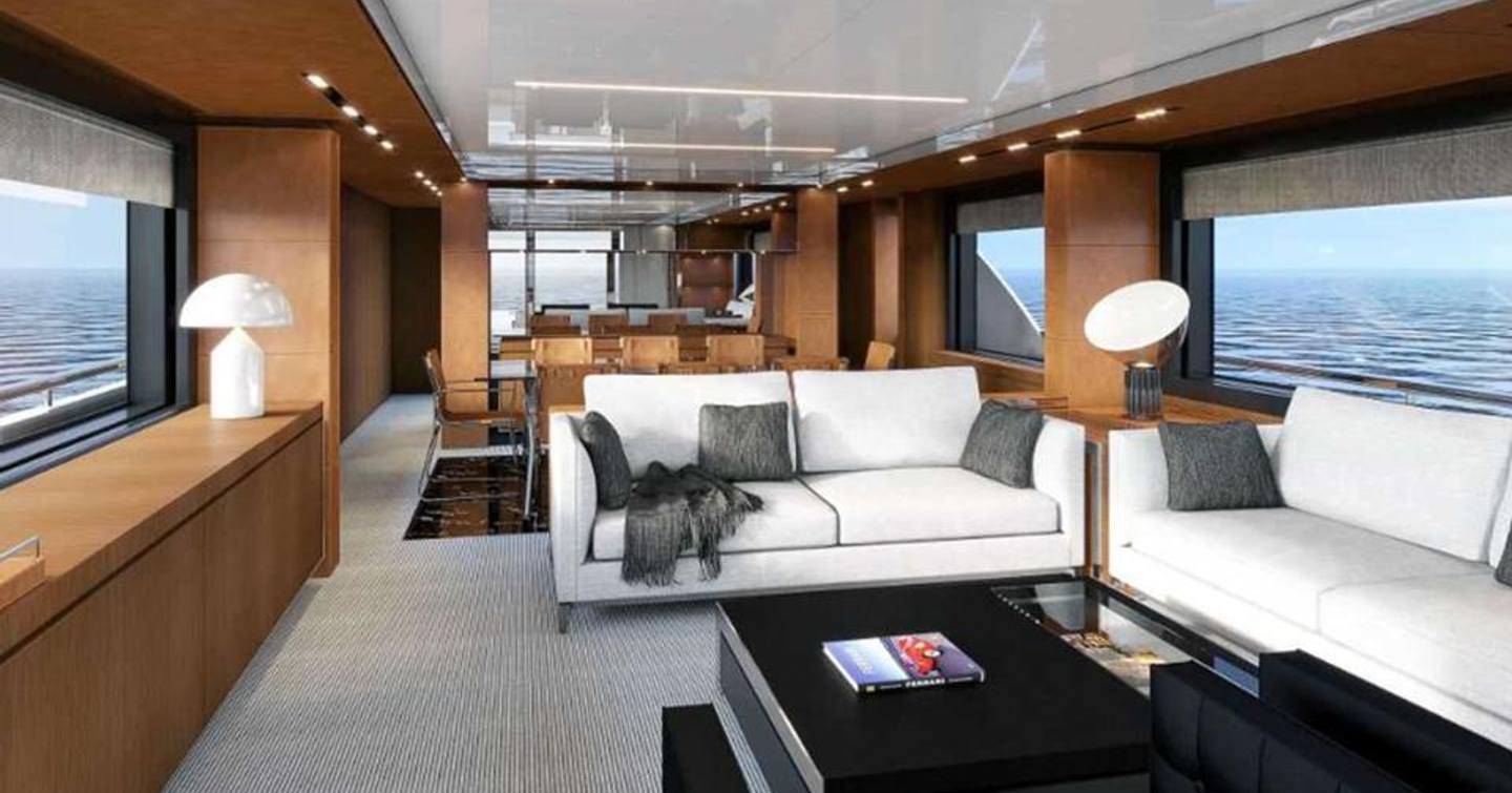 Long view of Riva Corsaro 100 Flybridge main salon living area, with two white sofas to the side accompanied by a black coffee table and multiple windows.