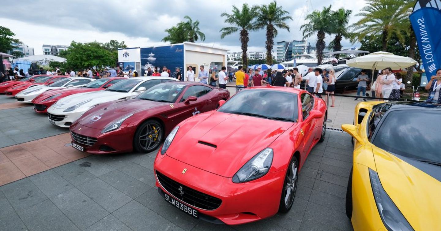 Row of sports cars on display at Singapore Yacht Show, visitors gathered around the back looking at the vehicles.