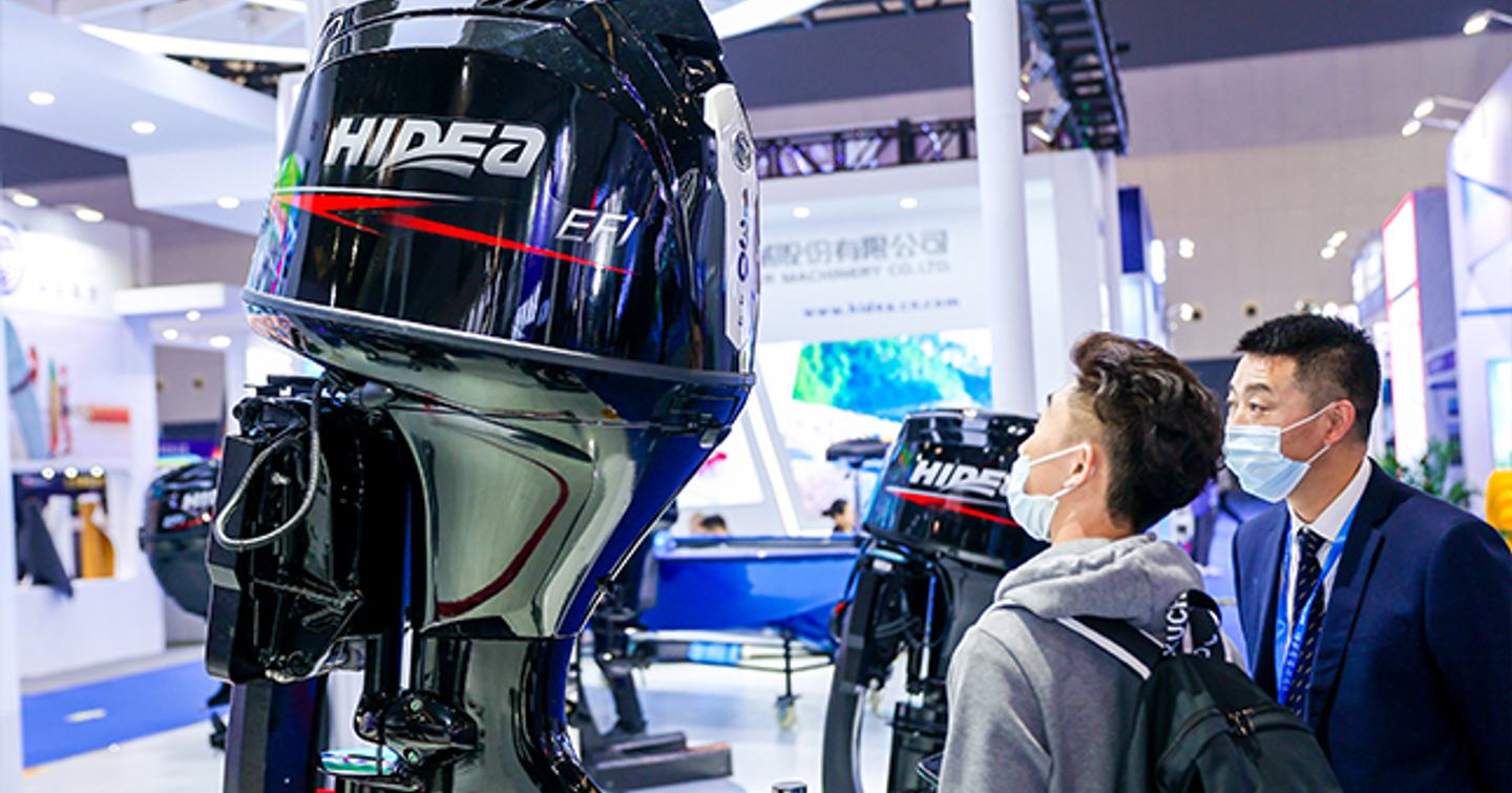 Visitors to the China International Boat Show stand viewing an outboard engine on display.