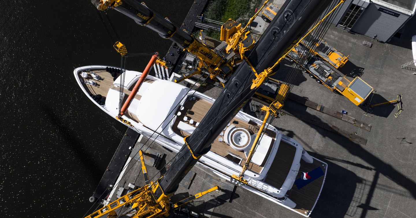 Aerial view of motor yacht Ad Astra during launch at the shipyard, with cranes lifting equipment above her teak decks and Jacuzzi
