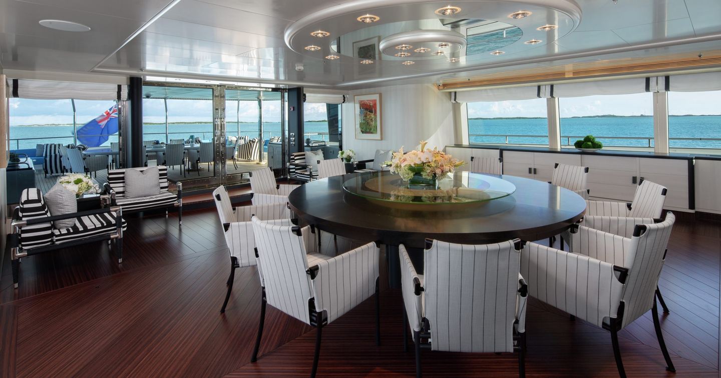 Superyacht Eternity upper deck salon with circular wooden dining table and glass sliding doors 