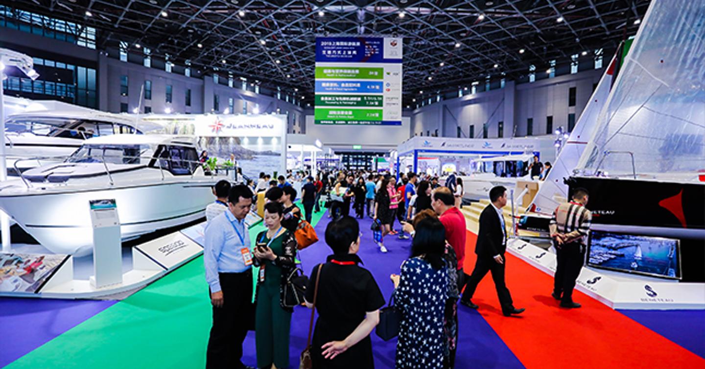 Visitors to the China International Boat Show standing on the carpet at the event, with motor yachts to port side and sailing boats to starboard.