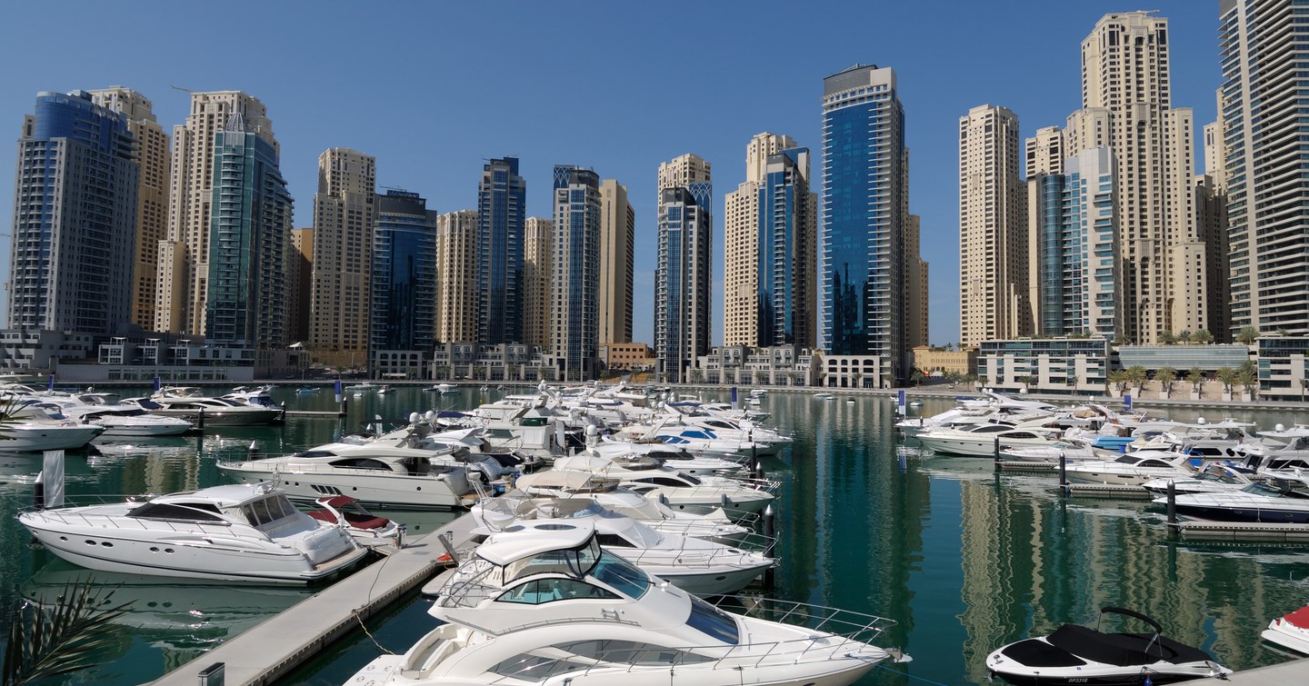 Overview of Dubai Harbour, with many motor yachts moored in front of Dubai skyscrapers