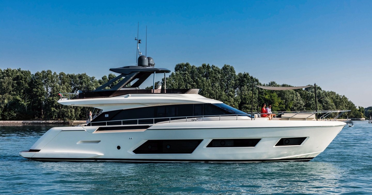 Side view of the Ferretti Yachts 670 anchored in front of green foliage.