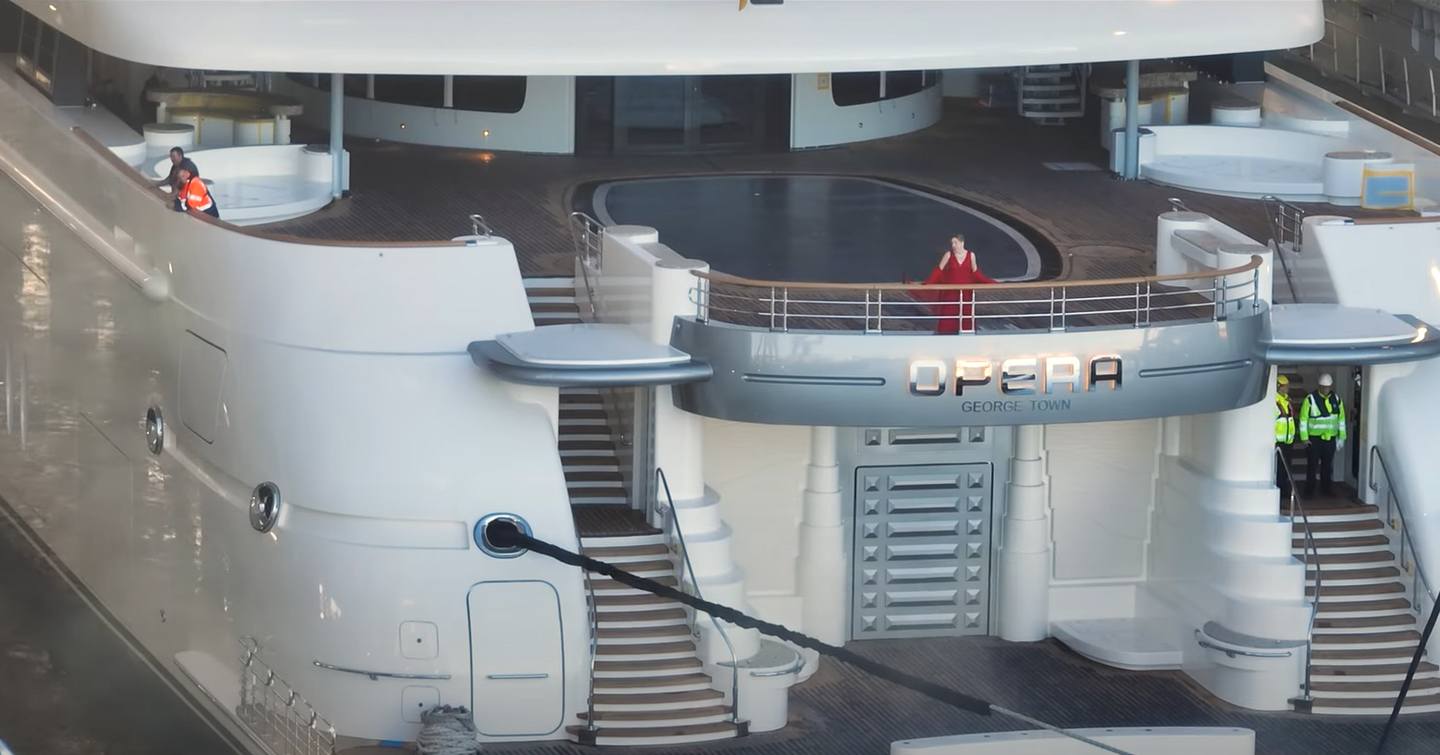 Aft view of Lurssen superyacht OPERA, crew members leaning over railings, with OPERA nameplate central.