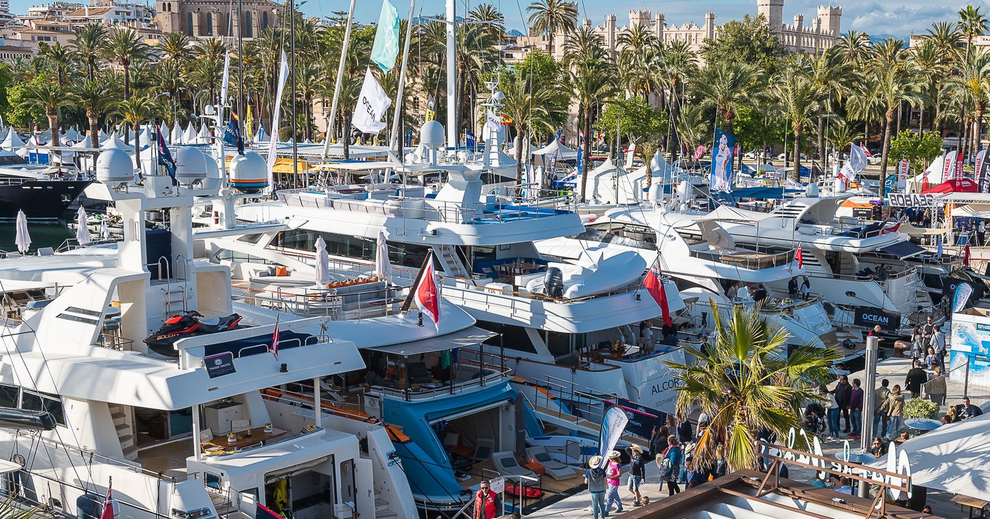 Motor yachts berthed in line at the Palma Superyacht Show. Visitors walking along boardwalk behind them.