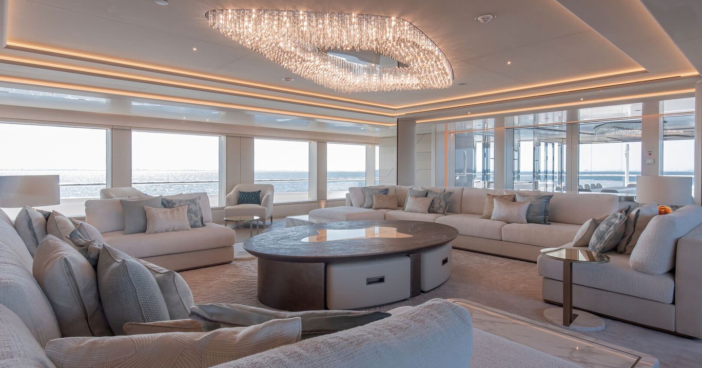 Overview of the main salon onboard superyacht H3, ample seating arranged around the oustide of the room, with vast stretches of glazing.