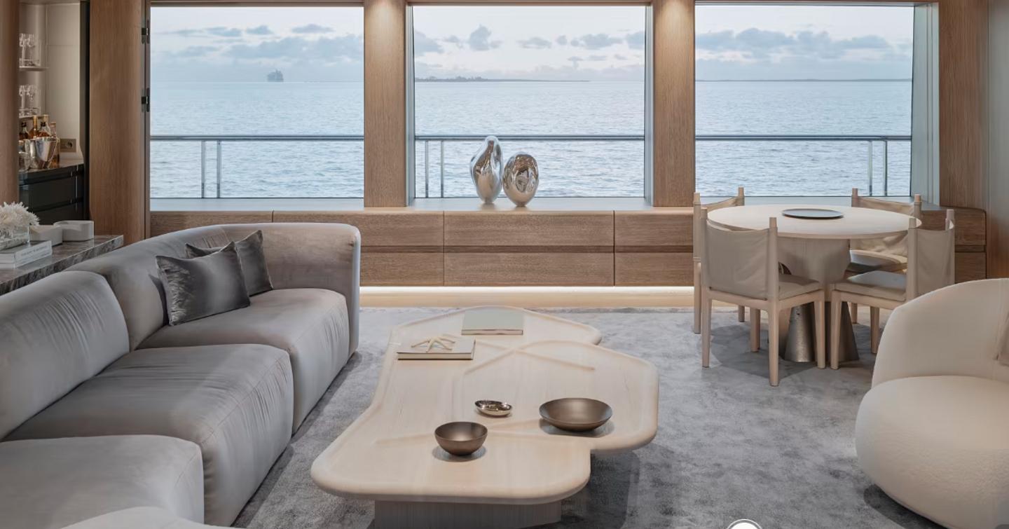 Overview of the main salon onboard superyacht ENTOURAGE. Long sofa to port side with extensive glazing in background and a small circular table with chairs.