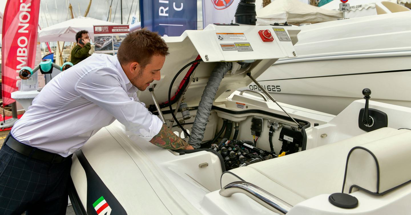 An exhibitor at the Palma International Boat Show inspecting an engine inside a displaying tender for sale