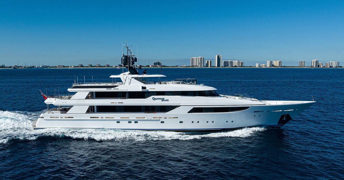 Side view of M/Y Quantum of Solace underway at sea, with cosmopolitan skyline in far distance.