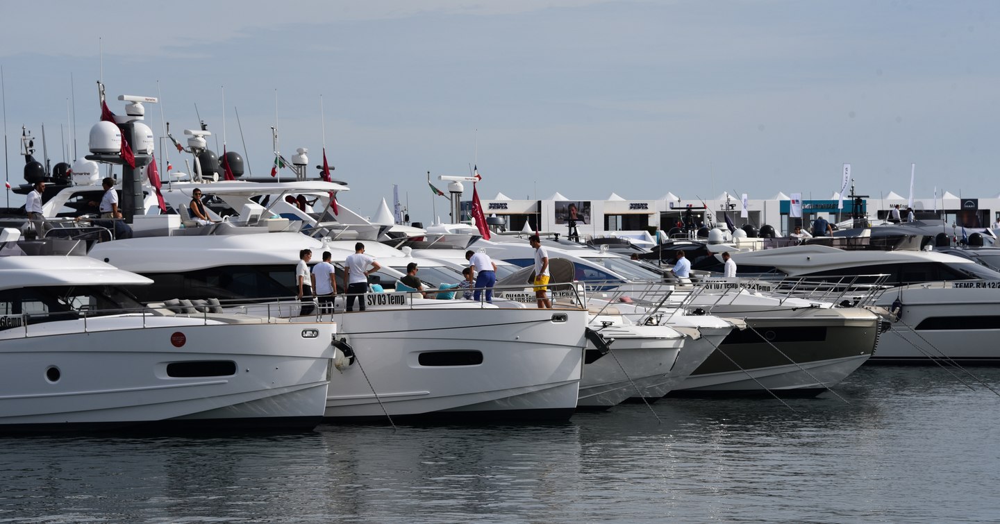 Line of motor yachts berthed at Cannes Yachting Festival, visitors exploring the yacht bows.