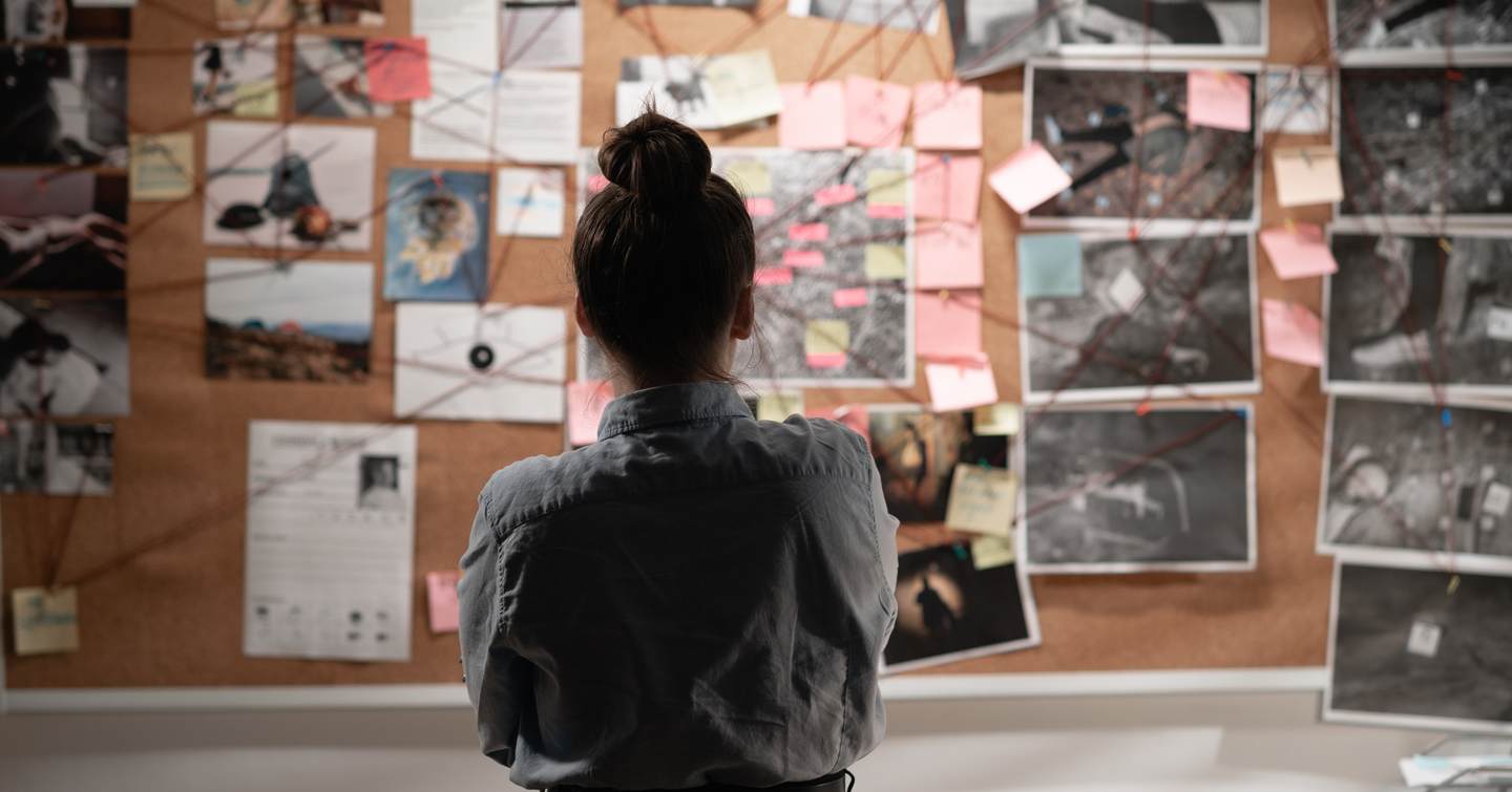 Female detective looking attentively at investigation board, back view