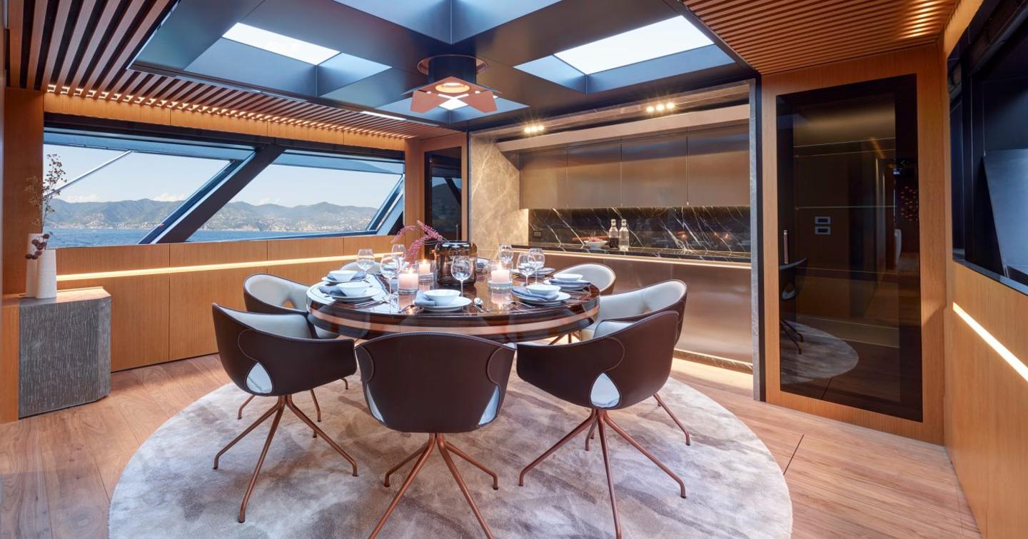 Overview of dining area onboard superyacht Blue Jeans. Circular dining table with six chairs central, with glazing to portside.