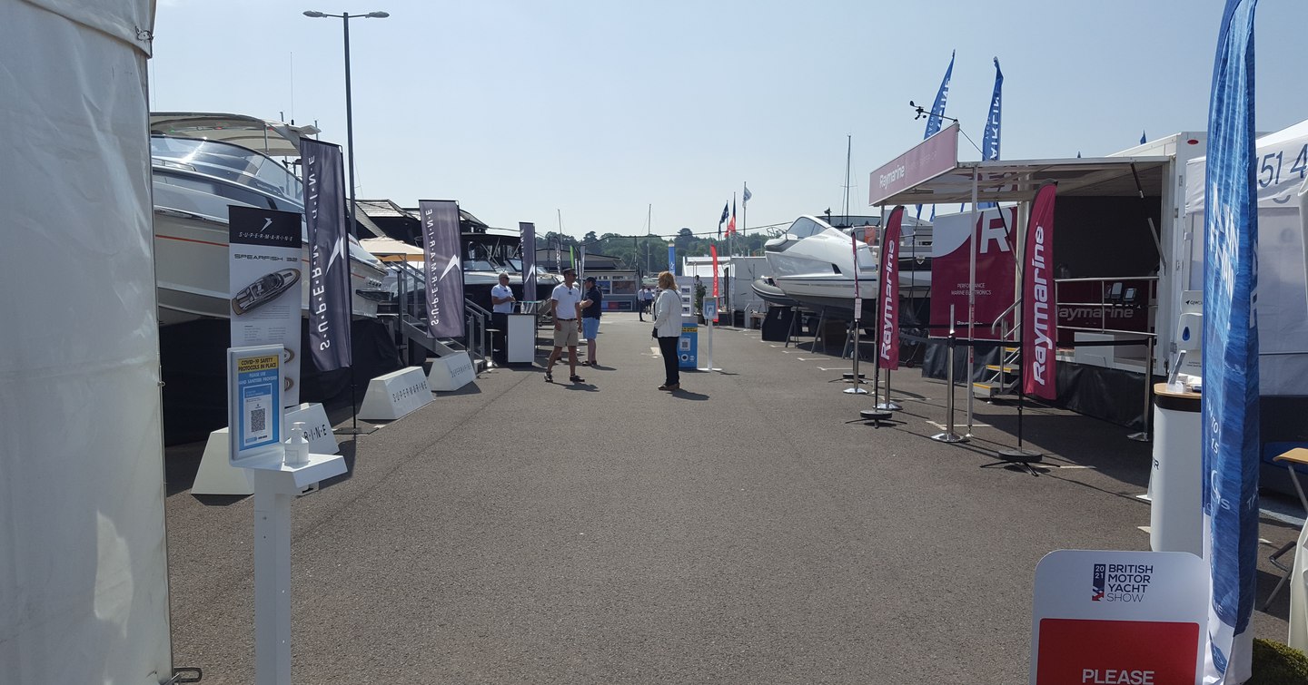 Exhibitor stands  at British Motor Yacht Show, couple of visitors in discussion along walkway.