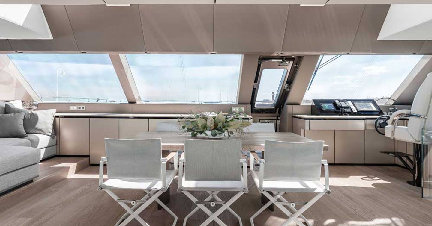 Three chairs in front of table inside yacht with sun shining through windows above