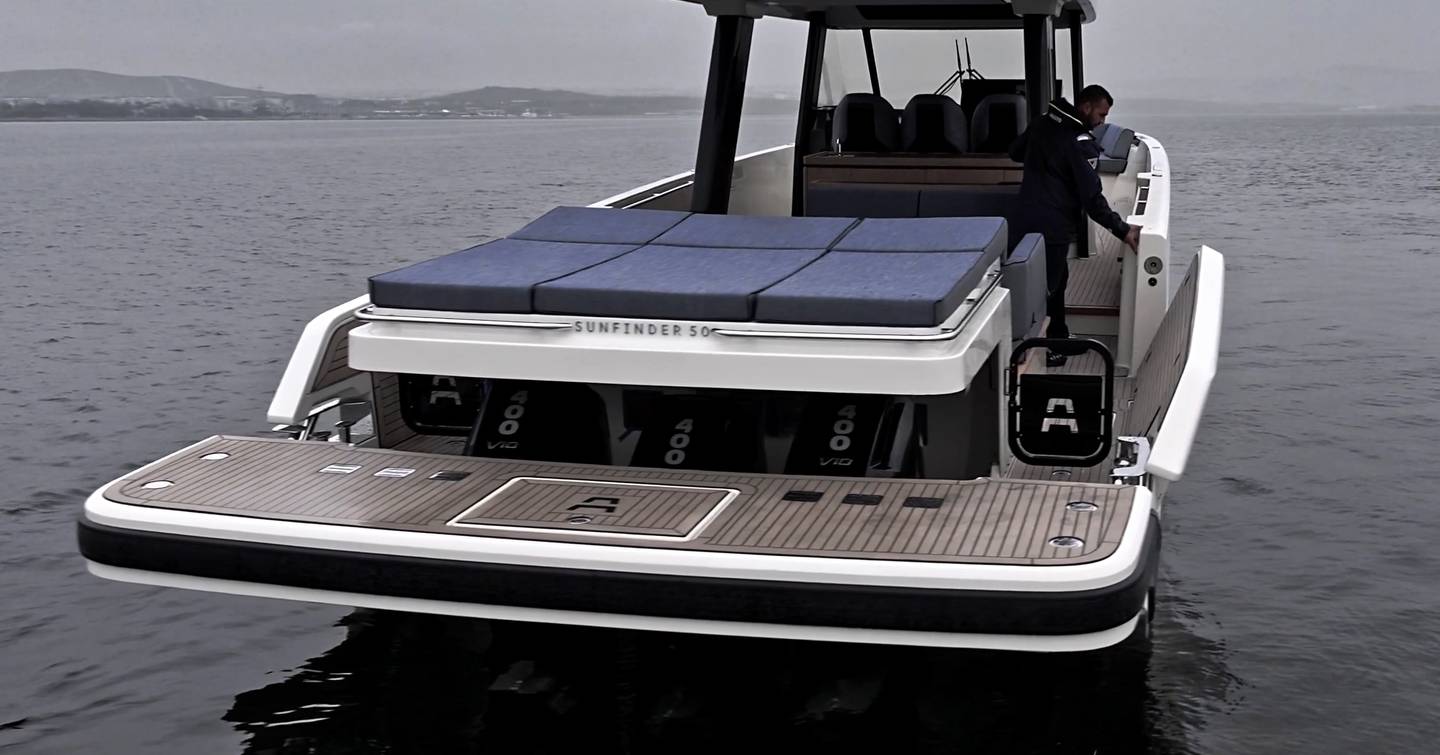 Stern view of the Aiata Sunfinder 50 at rest, showing the triple outboards, sun pad above and one side balcony folding down.