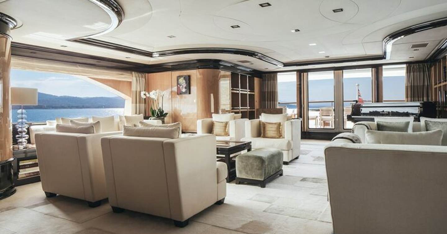 Overview of the main salon onboard M/Y MEAMINA, white armchairs and sofas facing in, surrounded by large windows.