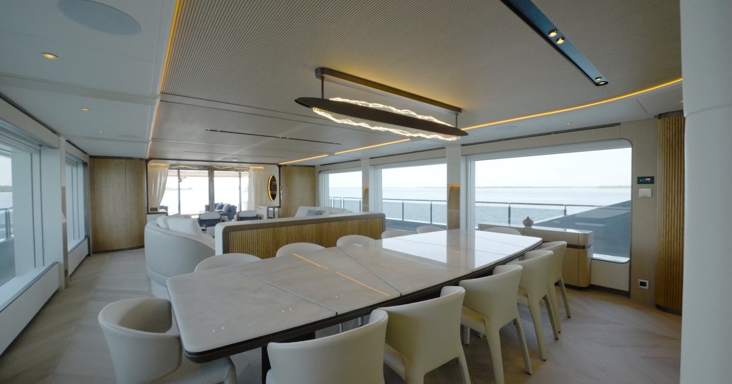 Main deck saloon aboard the Gulf Craft Majesty 145 with 12-seat dining area, curved lounge and panoramic glazing