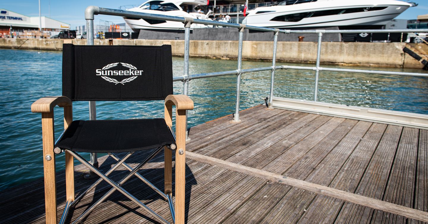 Solo director's chair reading Sunseeker sits on a waterfront boardwalk with motor yachts in background.