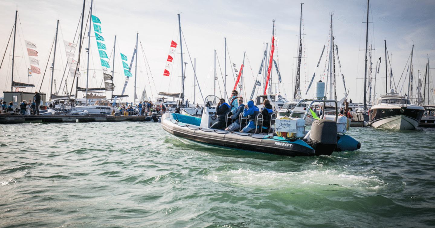 A RIB cruising along with onboard passengers, passing display of sailing boats at Southampton Boat Show.