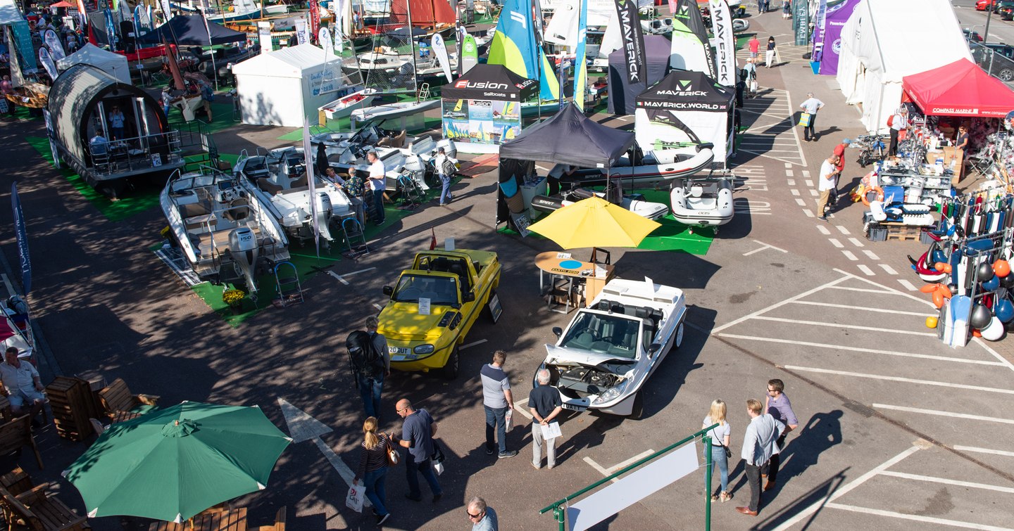 Mayflower Park at the Southampton Boat Show. Exhibitor stands and parasols throughout car park with visitors walking around.