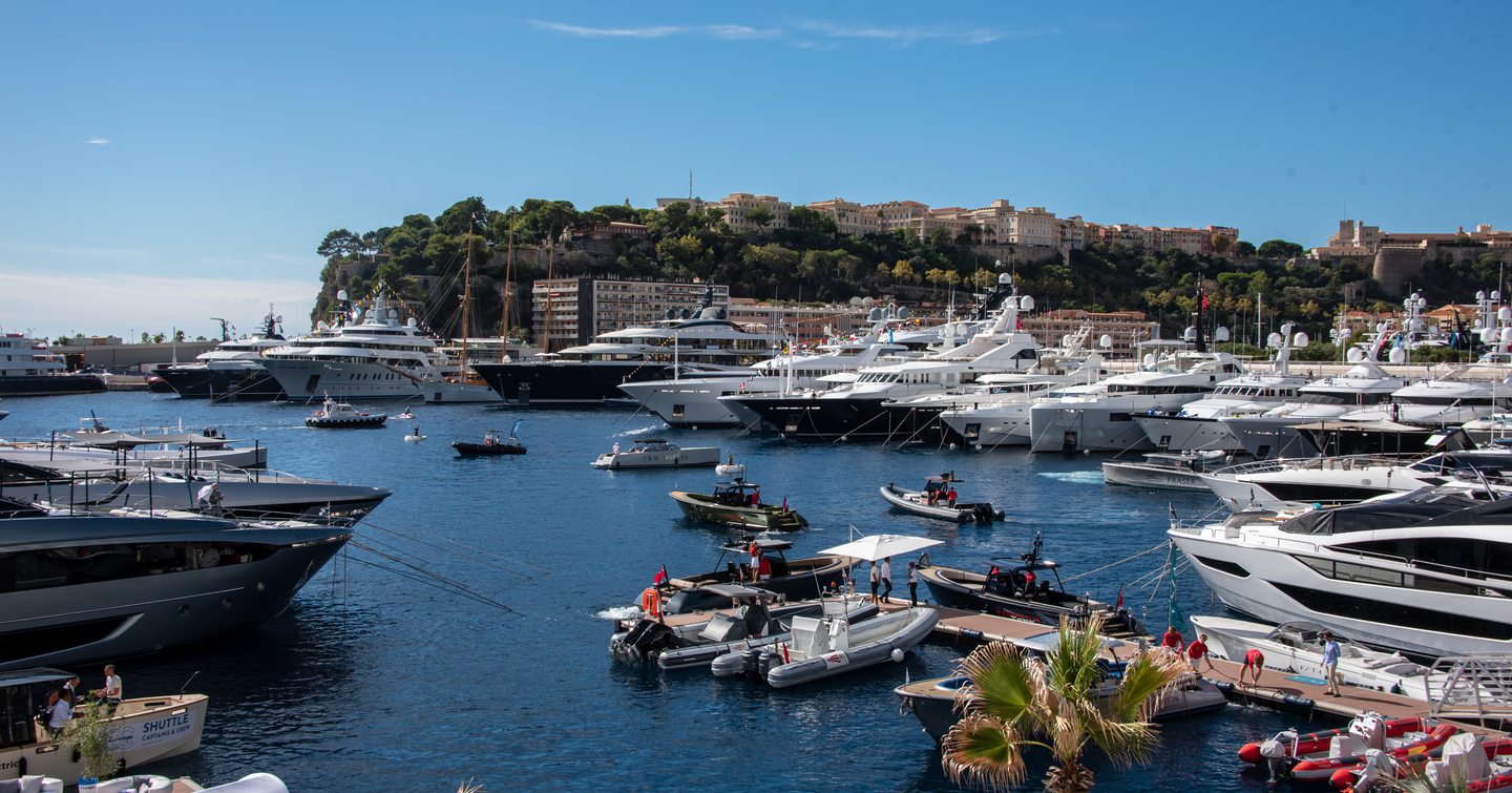 Overview of Port Hercule with many superyachts berthed. Several tenders and small craft milling about the bay.