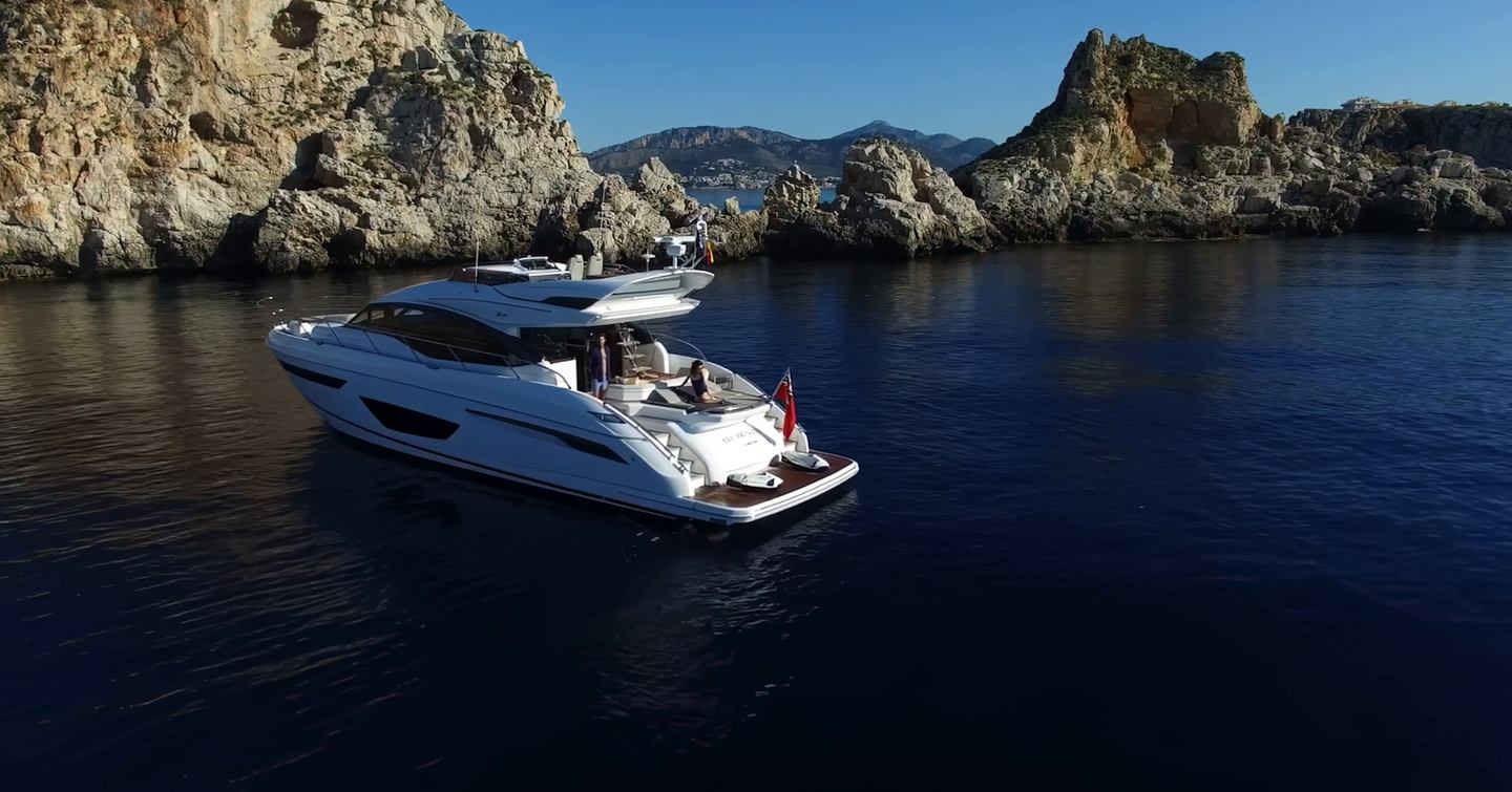 Princess S65 Mk2 sportsbridge yacht at anchor beside a rocky coastline, viewed from aft port quarter