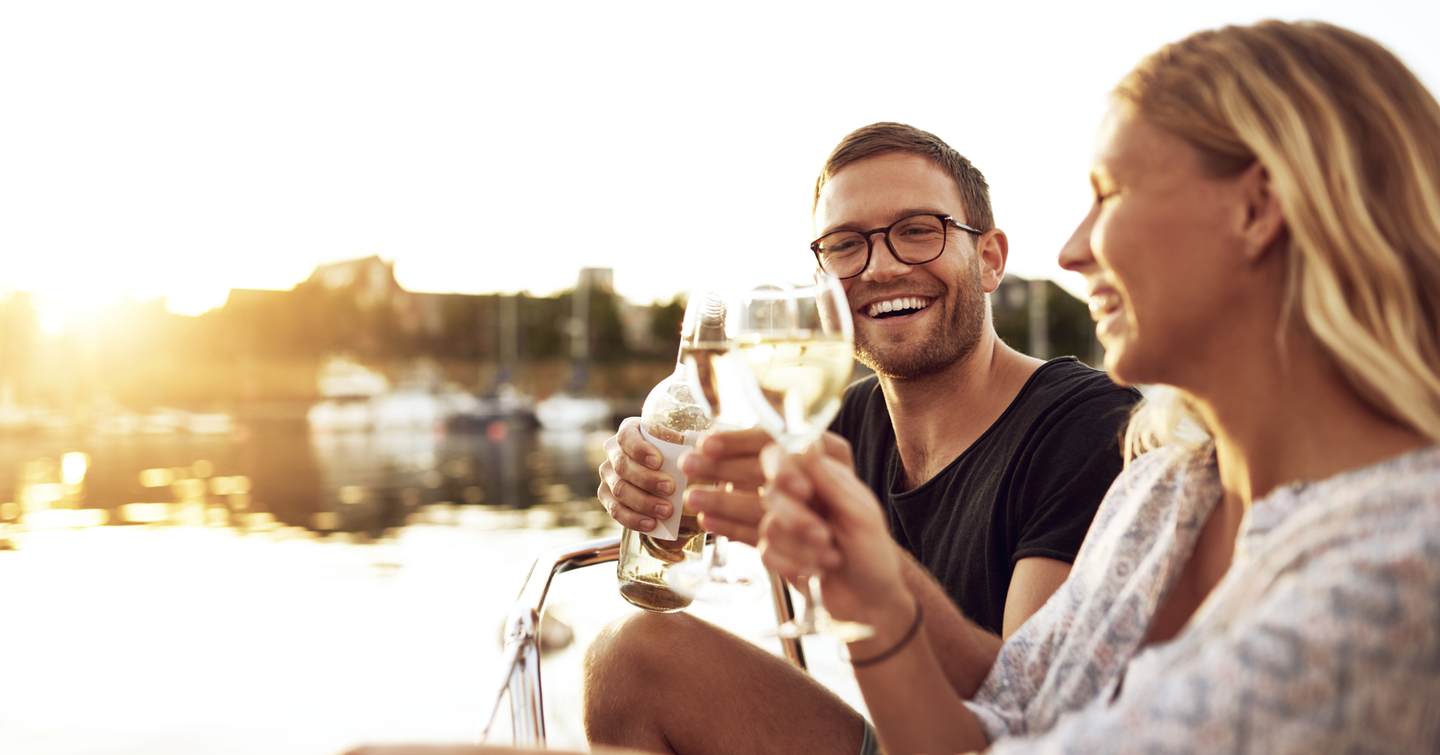 Couple sat on a yacht smiling with a glass of wine 