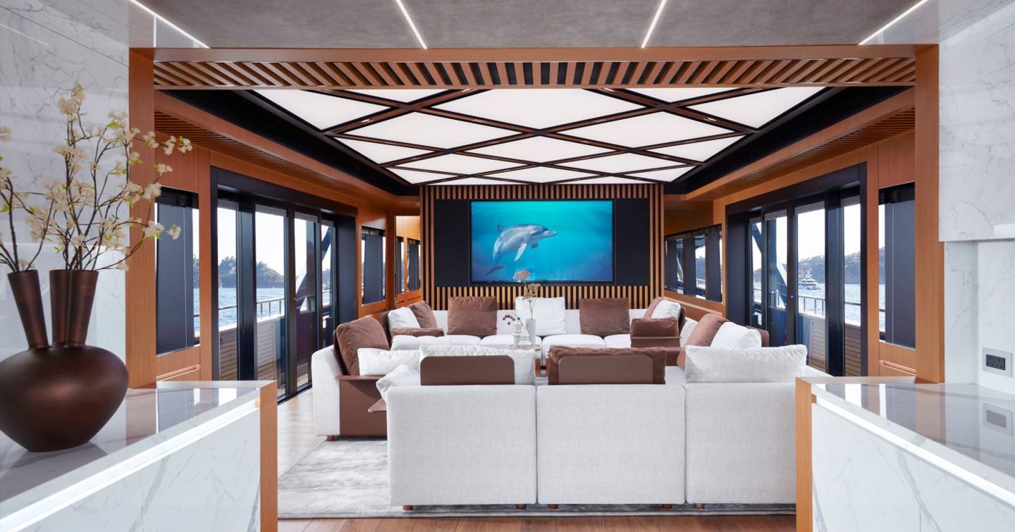 Overview of main salon onboard superyacht Blue Jeans. Central coffee table surrounded by cream seating, with stretches of glazing either side.