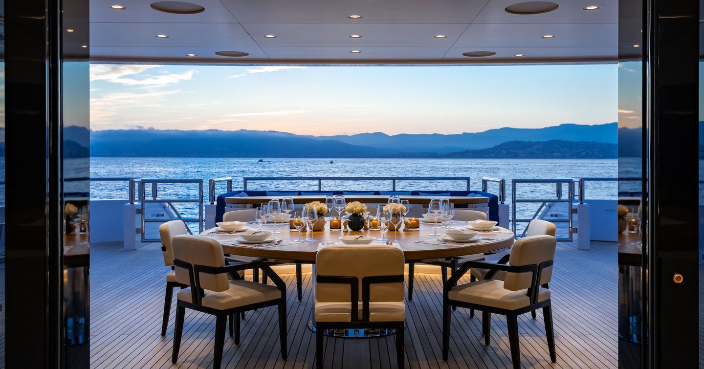 Exterior dining area onboard superyacht SOARING, large table surrounded by white seats, overlooking views of the sea.