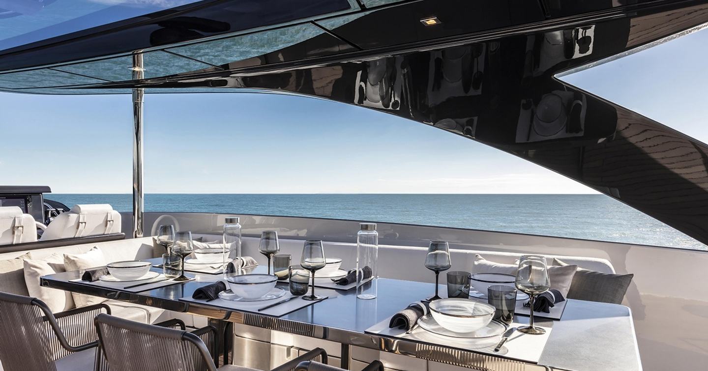 metallic table set for dinner under the hardtop of the Argo 90 with calm sea and clear blue sky in the background