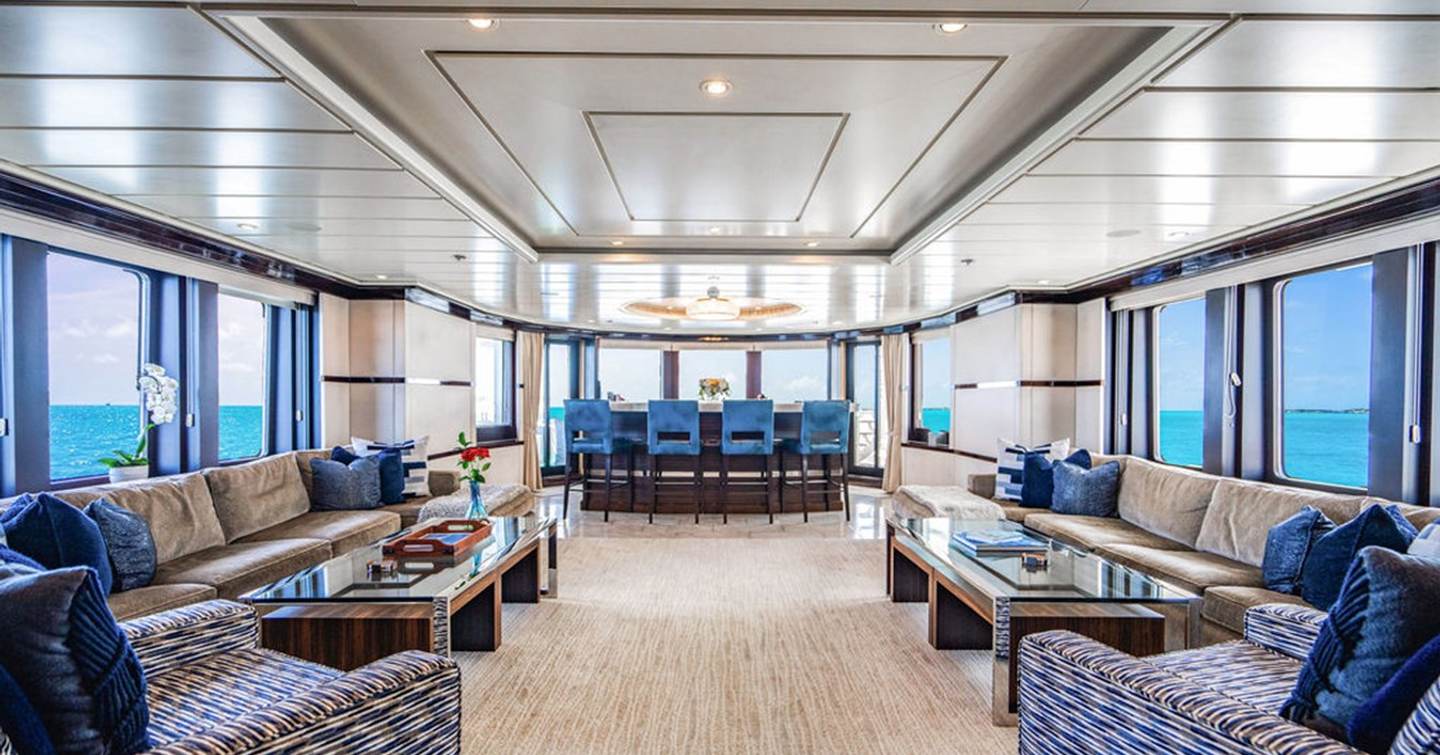 Motor yacht Nita K II's skylounge with dark bluer furnishings and mahogany bar area with panoramic windows and sea views