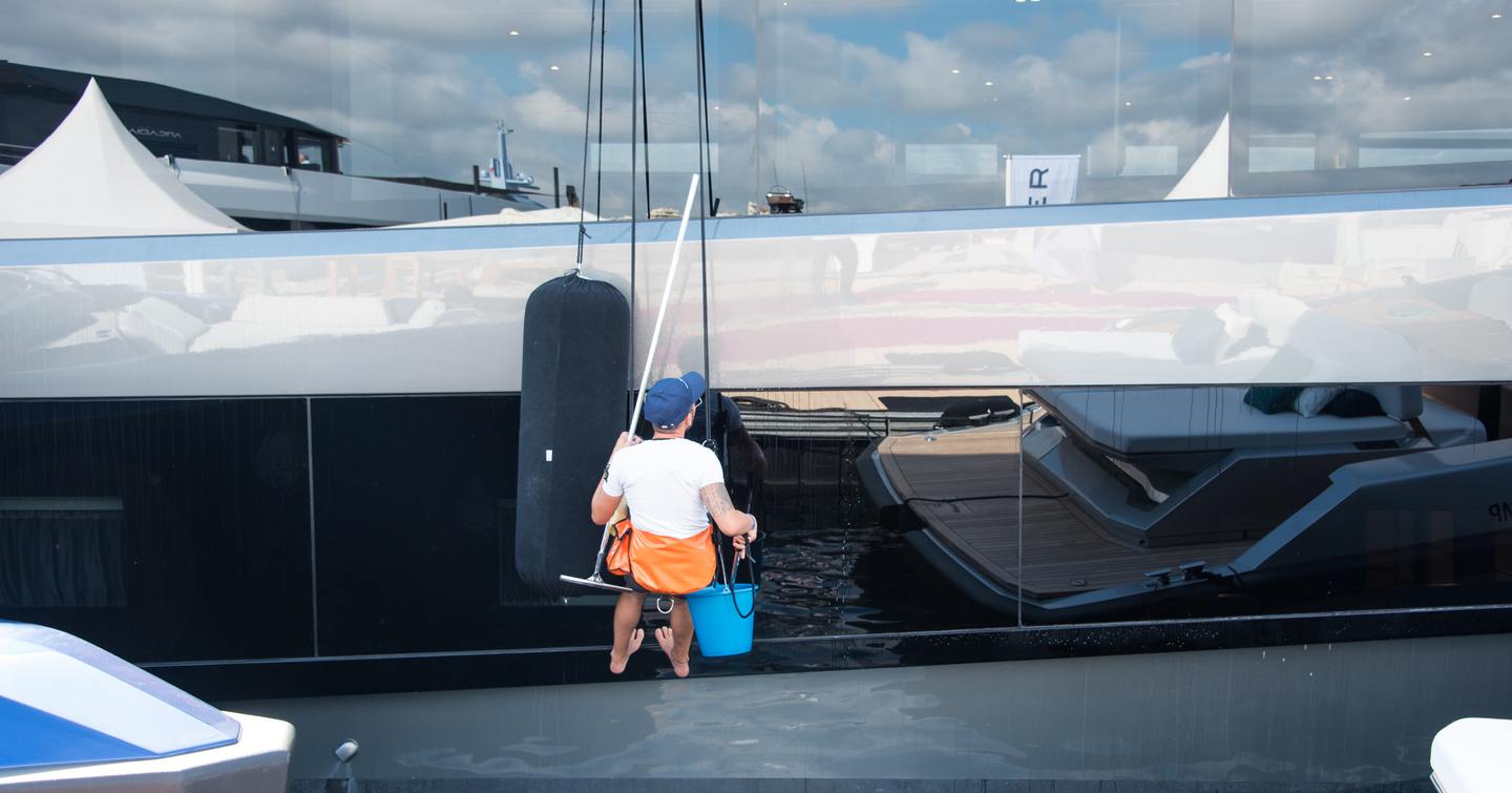 Crew member cleaning hull of moored superyacht